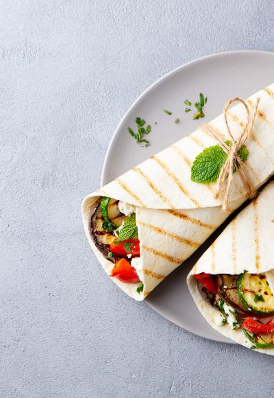 Wrap sandwich with grilled vegetables and feta cheese on a plate. Grey background. Copy space. Top view.