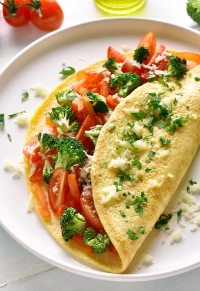 Omelet with tomatoes, red bell pepper and broccoli on light wooden table. Healthy diet food for breakfast. Tasty morning food.