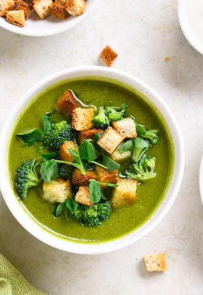 Healthy broccoli green pea cream soup with croutons in bowl over light stone background. Diet detox food concept. Top view, flat lay