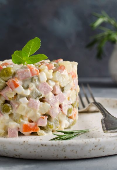 Russian traditional salad Olivier with vegetables and meat. Salad on a plate on a gray stone background