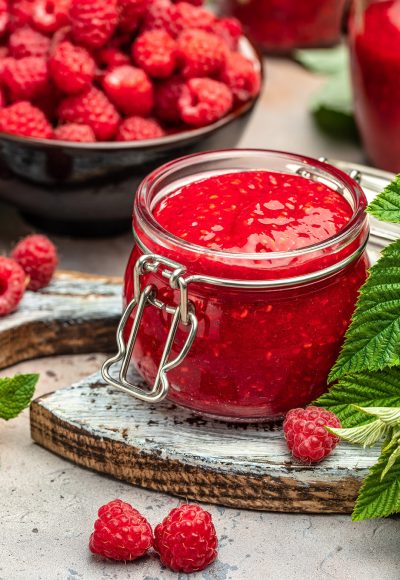 Homemade raspberry jam in jar with raspberries and mint. vertical image. top view. place for text.