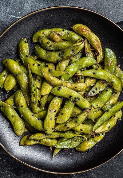 Stir-fried green Edamame Soy Beans with sea salt and sesame seeds in a plate. Black background. Top view.