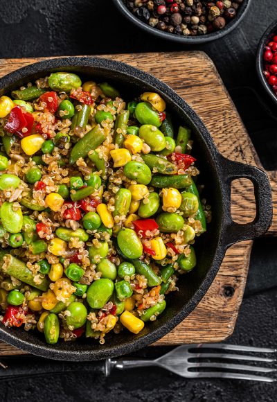 Vegetarian fried Quinoa salad with edamame, corn, carott, tomato, paprika, onions in a pan. Black background. Top view.