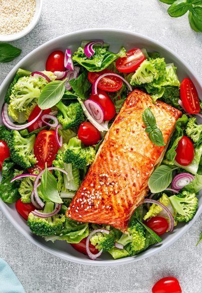 Grilled salmon fish fillet and fresh green leafy vegetable salad with tomatoes, red onion and broccoli. Healthy food. Ketogenic lunch. Top view