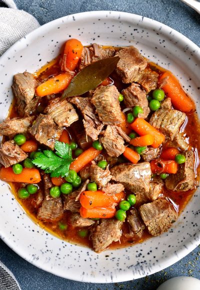 Meat stew with carrot and green pea in a white bowl over dark grey slate or stone background.Top view.