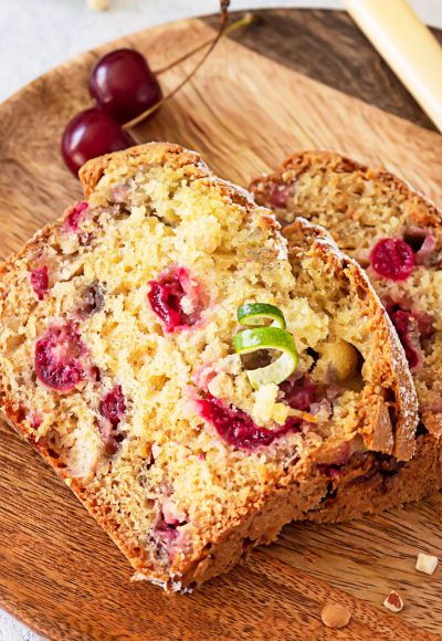 Homemade sweet cherry loaf cake with nuts on wooden plate. Light blue concrete background.