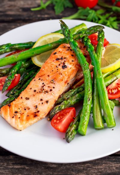 Fried salmon with asparagus, tomatoes, lemon, yellow lime on white plate