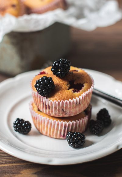 Homemade muffins with blackberry berries on a white plate on a brown wooden background