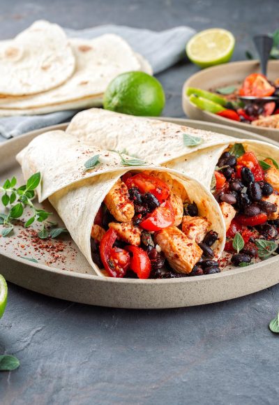 Mexican style burritos - tortilla wrap with spicy chicken meat breast filet filling, black beans, beans, olives, chopped tomatos