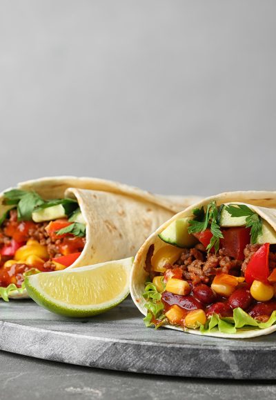 Board with delicious meat tortilla wraps on grey table