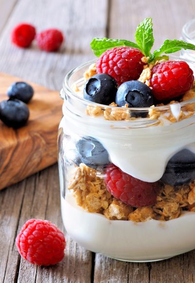 Blueberry and raspberry parfaits in mason jars, scene on a rustic wood background