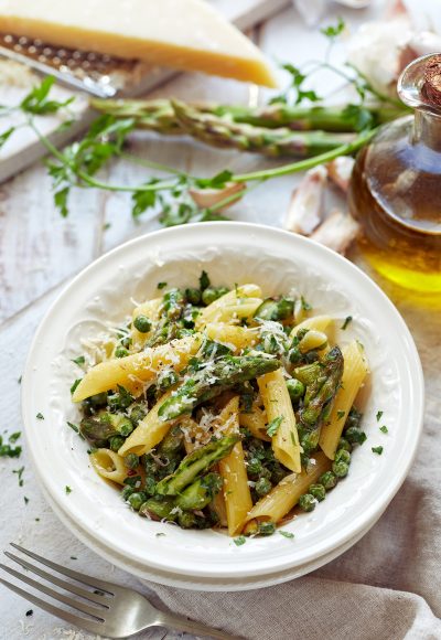 Penne pasta with green asparagus and peas sprinkled with grated Parmesan cheese, top view