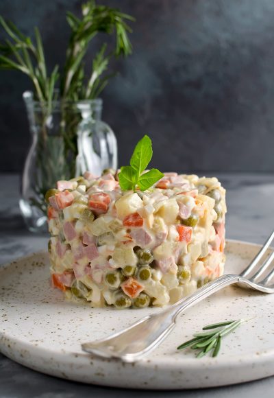 Russian traditional salad Olivier with vegetables and meat. Salad on a plate on a gray stone background