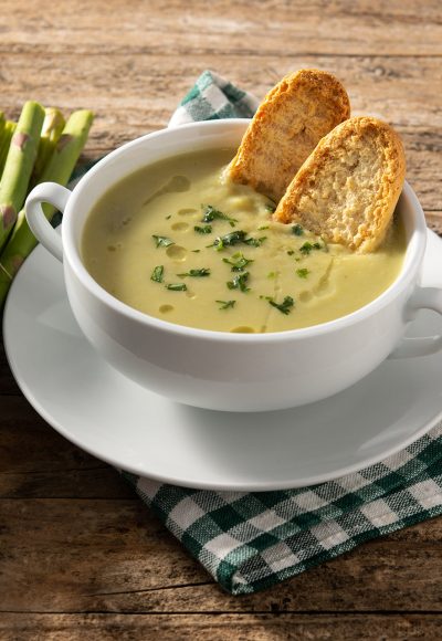 Fresh green asparagus soup in bowl on wooden table