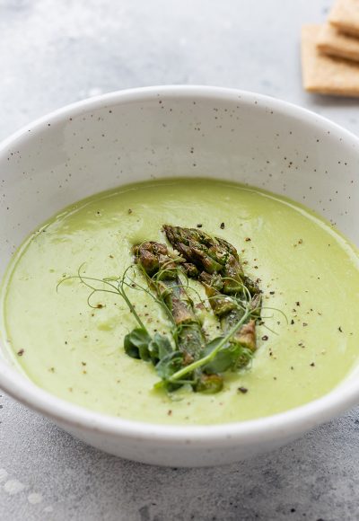 asparagus cream soup in ceramic bowl and rice crackers on gray table. Vegan, diet food