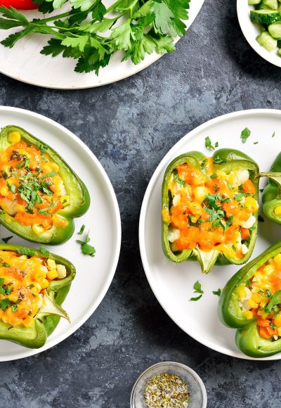 Baked green bell peppers filled with corn, carrot, cauliflower on white plate over blue stone background. Healthy diet or vegetarian food concept. Top view, flat lay