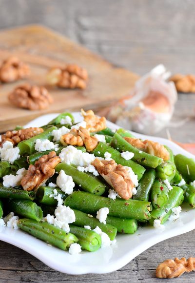 Green string beans salad with cottage cheese and walnuts on a white plate and old wooden table Closeup