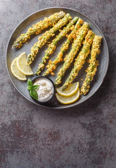 Crunchy baked asparagus fries with mayonnaise dip, healthy vegetable snack close-up on a plate on a table. Vertical top view from above