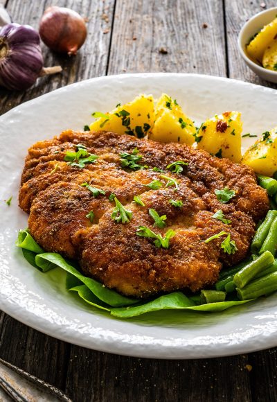 Breaded fried pork chop with green beans and potatoes on wooden table