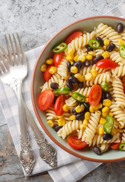 Fresh homemade colorful vegan fusilli pasta salad with beans, corn, tomato and jalapeno close-up in a plate on the table. Horizontal top view from above