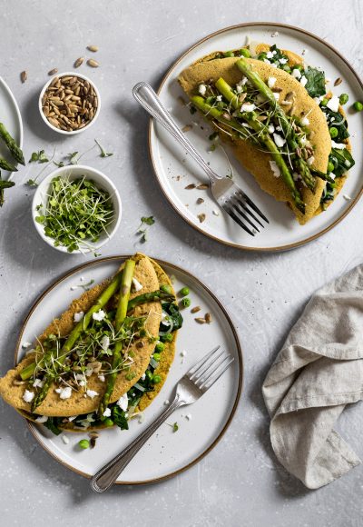 A view of a table with delicious, freshly made vegan crepes ready to be eaten. Made of nutirious chickpea flour, filled with spinach, peas and vegan cheese, topped with grilled asparagus and seeds