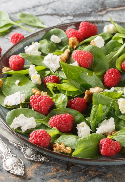 Dietary raspberry spinach salad with feta and walnuts with vinaigrette dressing close-up in a plate on the table. Horizontal