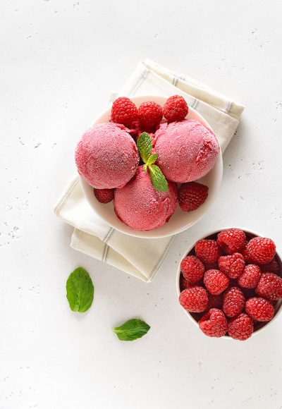 Homemade raspberry ice cream scoop in bowl and fresh berries over stone background with free text space. Top view, flat lay