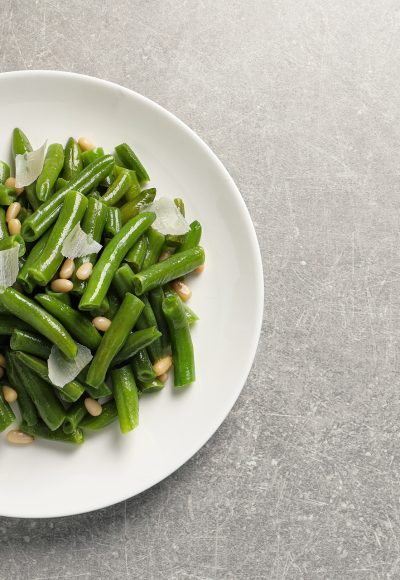 Plate of tasty salad with green beans on light grey table, top view. Space for text