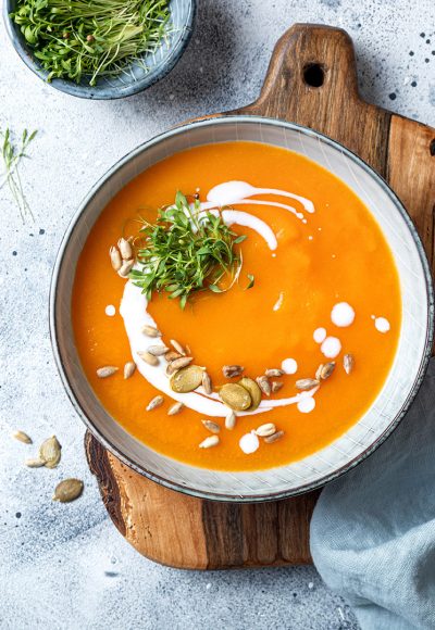 Vegetarian autumn pumpkin and carrot soup with cream, seeds and cilantro micro greens. Comfort food, fall and winter healthy slow food concept