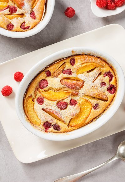 Traditional french pie clafoutis with fresh summer peaches and raspberry. Light- gray stone background, top view