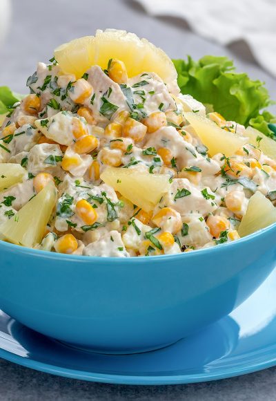 Chicken salad with pineapple and corn served in a blue bowl on a light background.