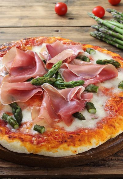 Italian pizza with ham and asparagus on rustic table background