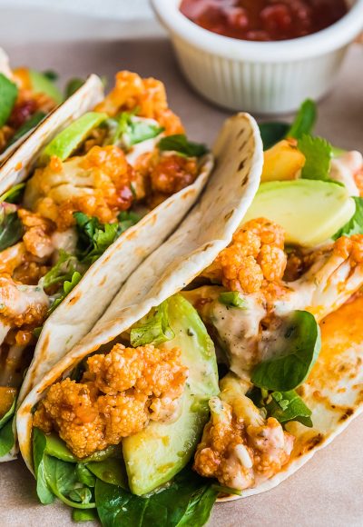 Vegan tacos with cauliflower, avocado and cilantro with sauces on a light background